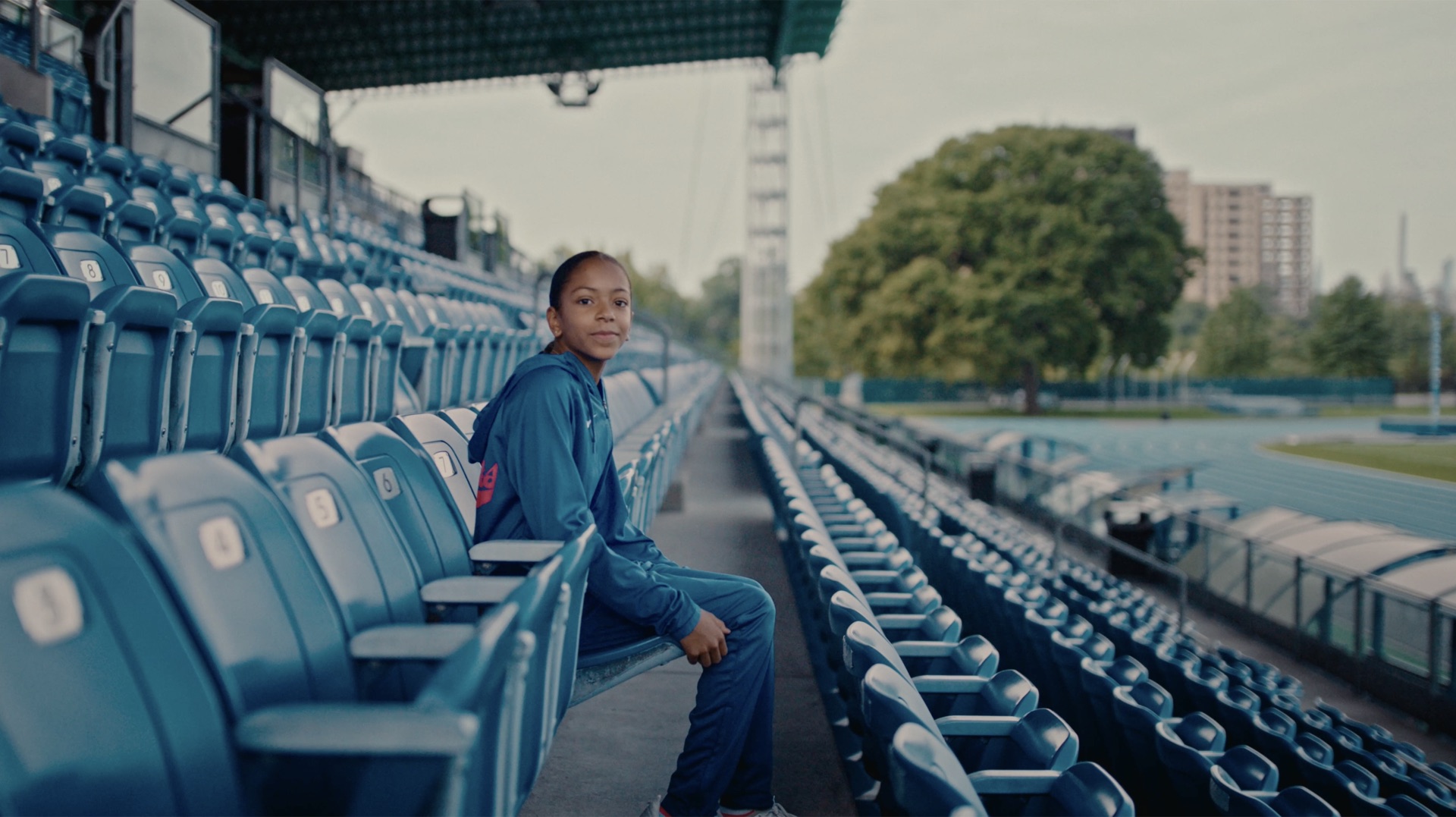 Young athlete in a blue tracksuit walking the track, city skyline in the background