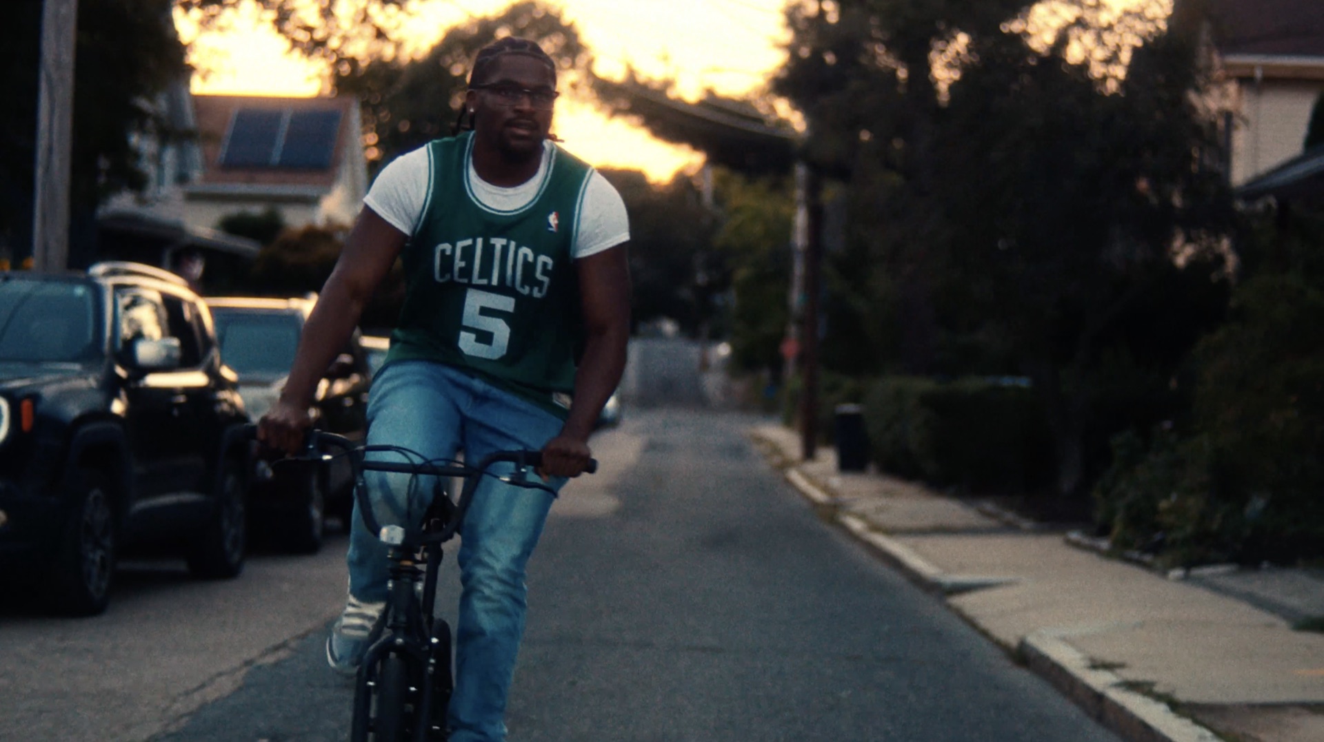 Man riding a bike in a Celtics jersey, golden hour, facing camera