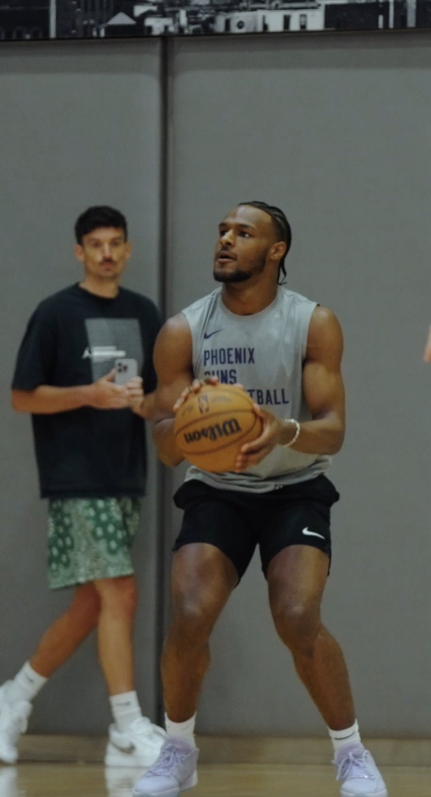 A Phoenix Suns player shooting as a teammate films on his phone