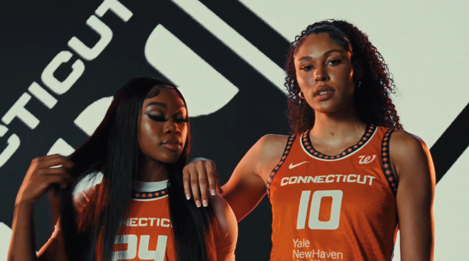 Player pulling open her white SUN No. 24 jersey against an orange street-map backdrop