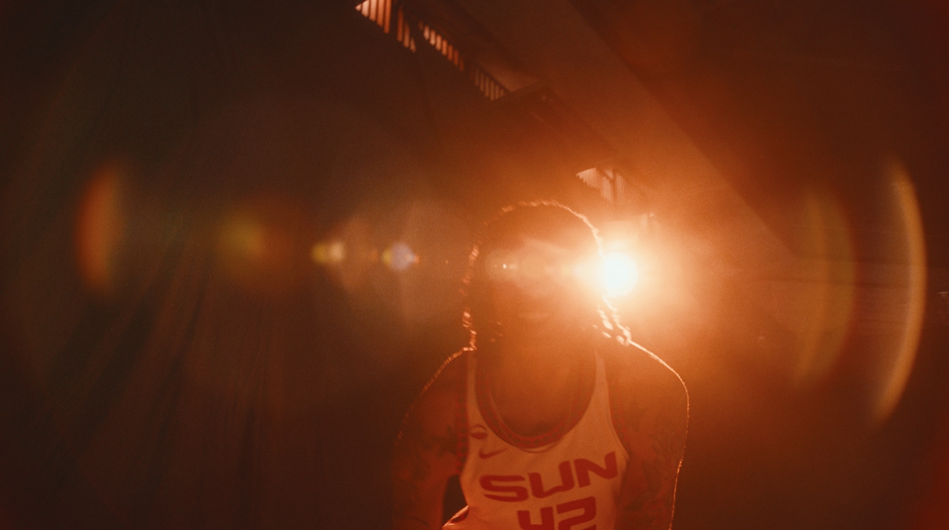 Player silhouetted in a SUN No. 42 jersey walking toward a bright lens flare in a tunnel