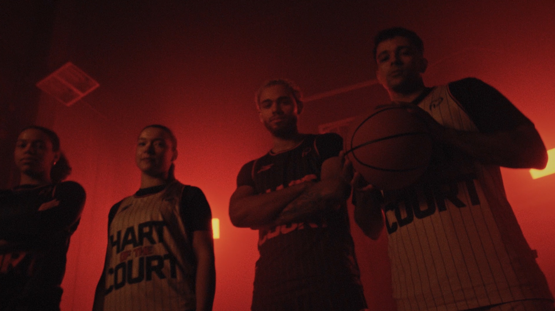 Four teammates lit in deep red, one wearing a HART OF THE COURT jersey
