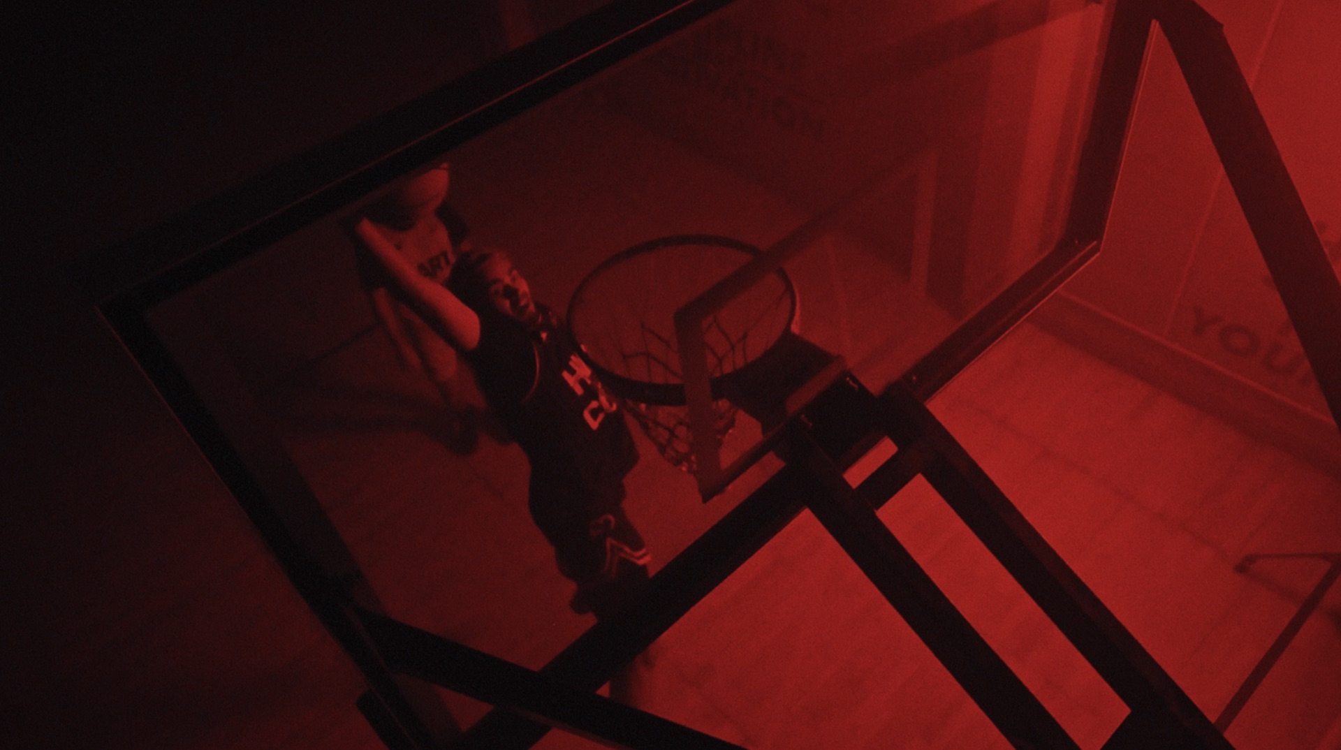 Low-angle shot through the backboard of a player dunking, bathed in red light