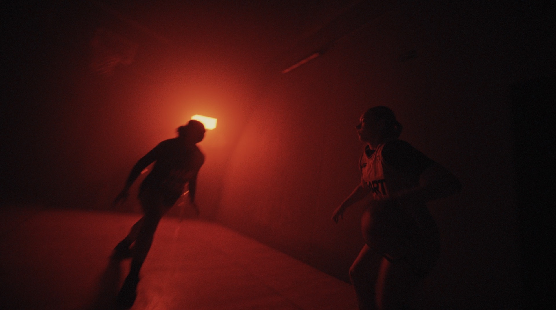 Two players silhouetted in a dark, red-lit room with a glowing light source