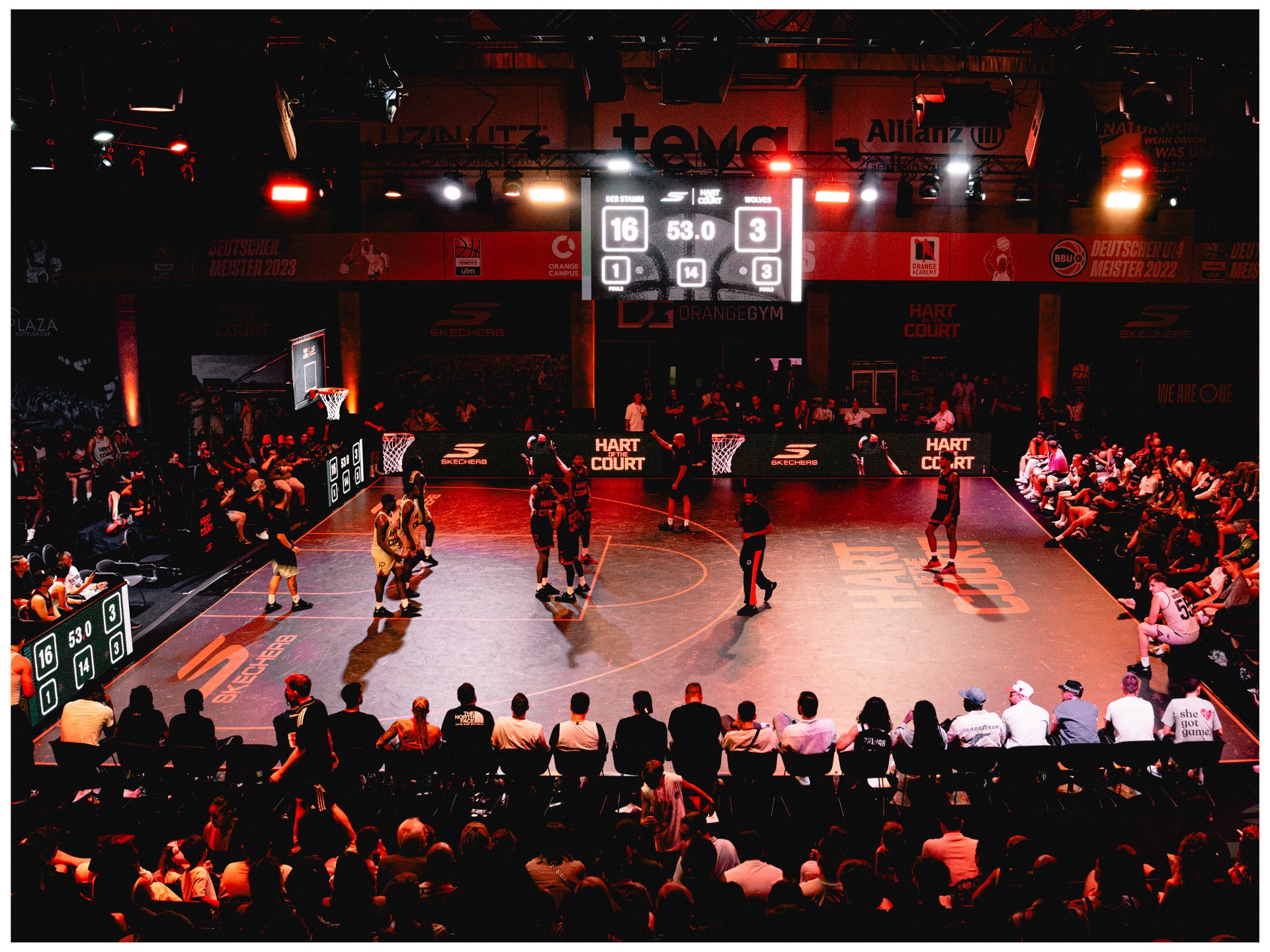 Wide shot of the tournament court packed with fans, scoreboard reading 16-3 under red stage lighting