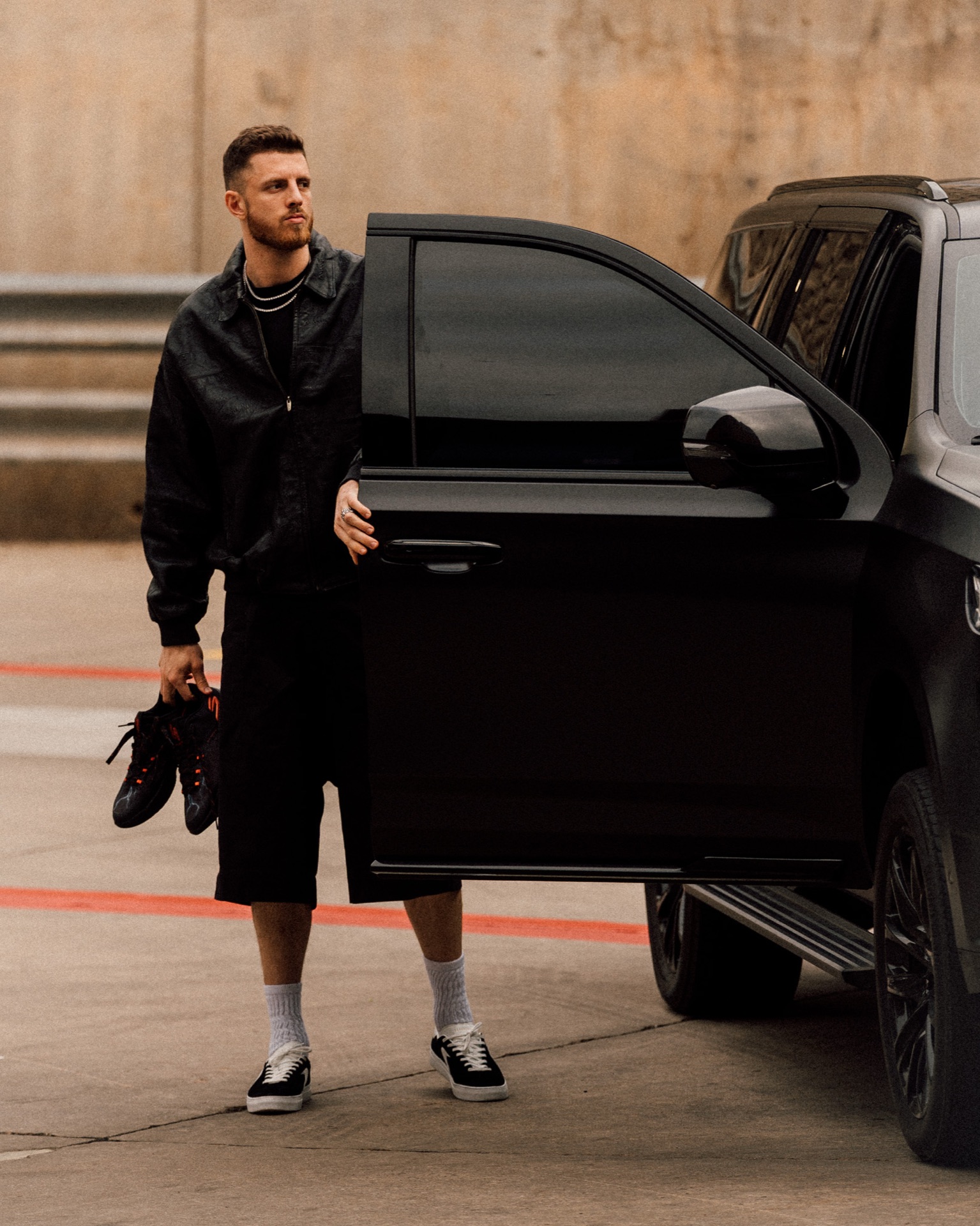 Isaiah Hartenstein holding sneakers, stepping out of a black SUV in a leather jacket