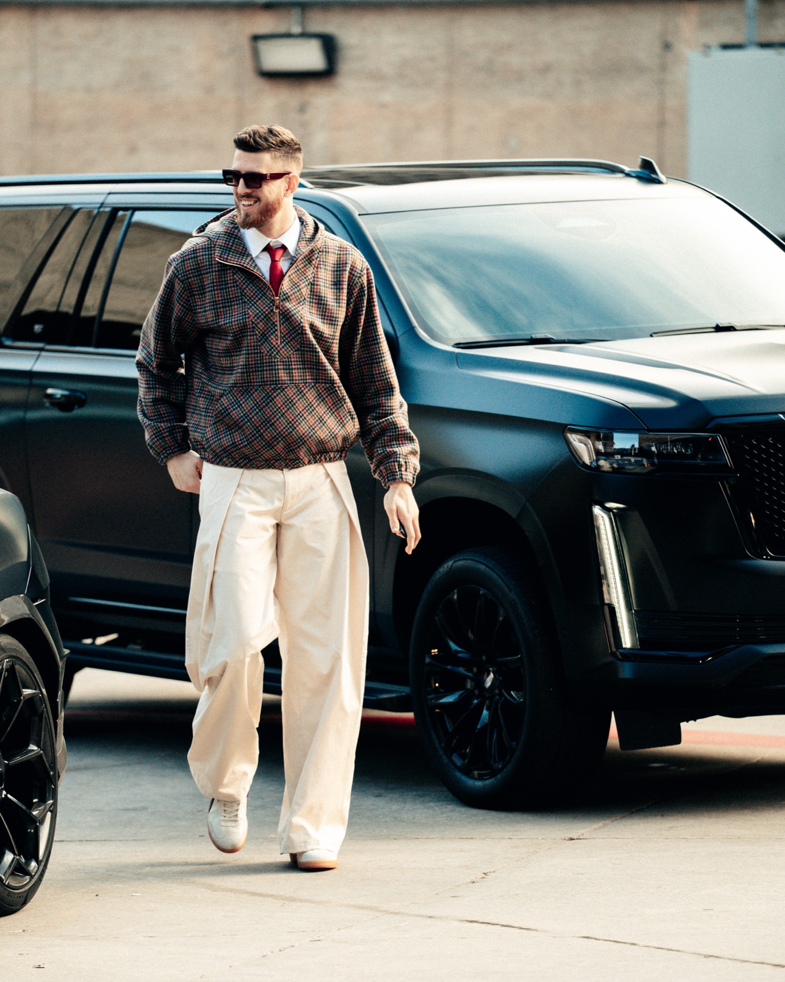 Isaiah Hartenstein in a plaid jacket, dress shirt and tie, smiling beside a matte black SUV