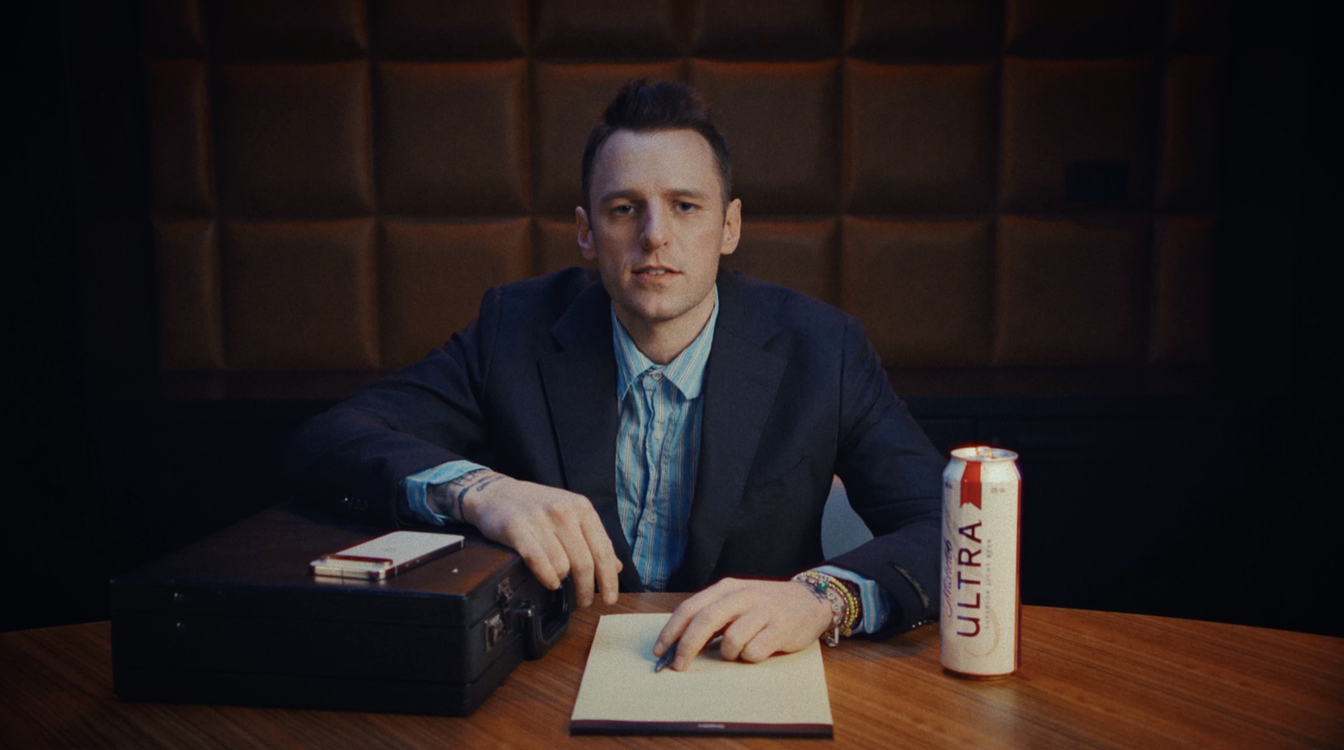 Man in a suit at a booth table with a briefcase and a Michelob Ultra can