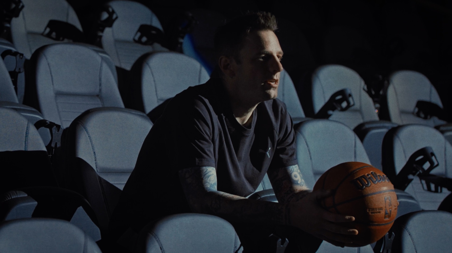 Portrait in empty arena seats, side profile, holding a basketball