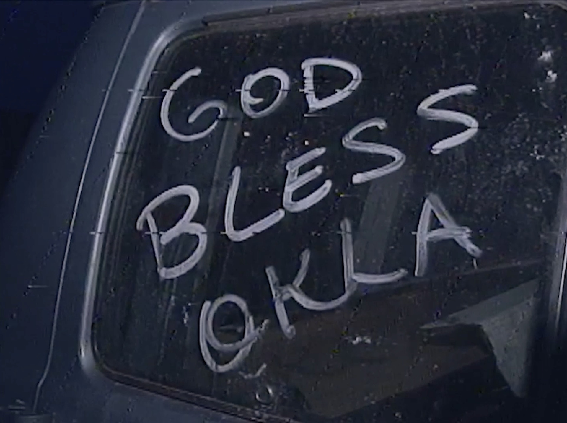 Archival image: "God Bless Okla" written in the dust on a vehicle window