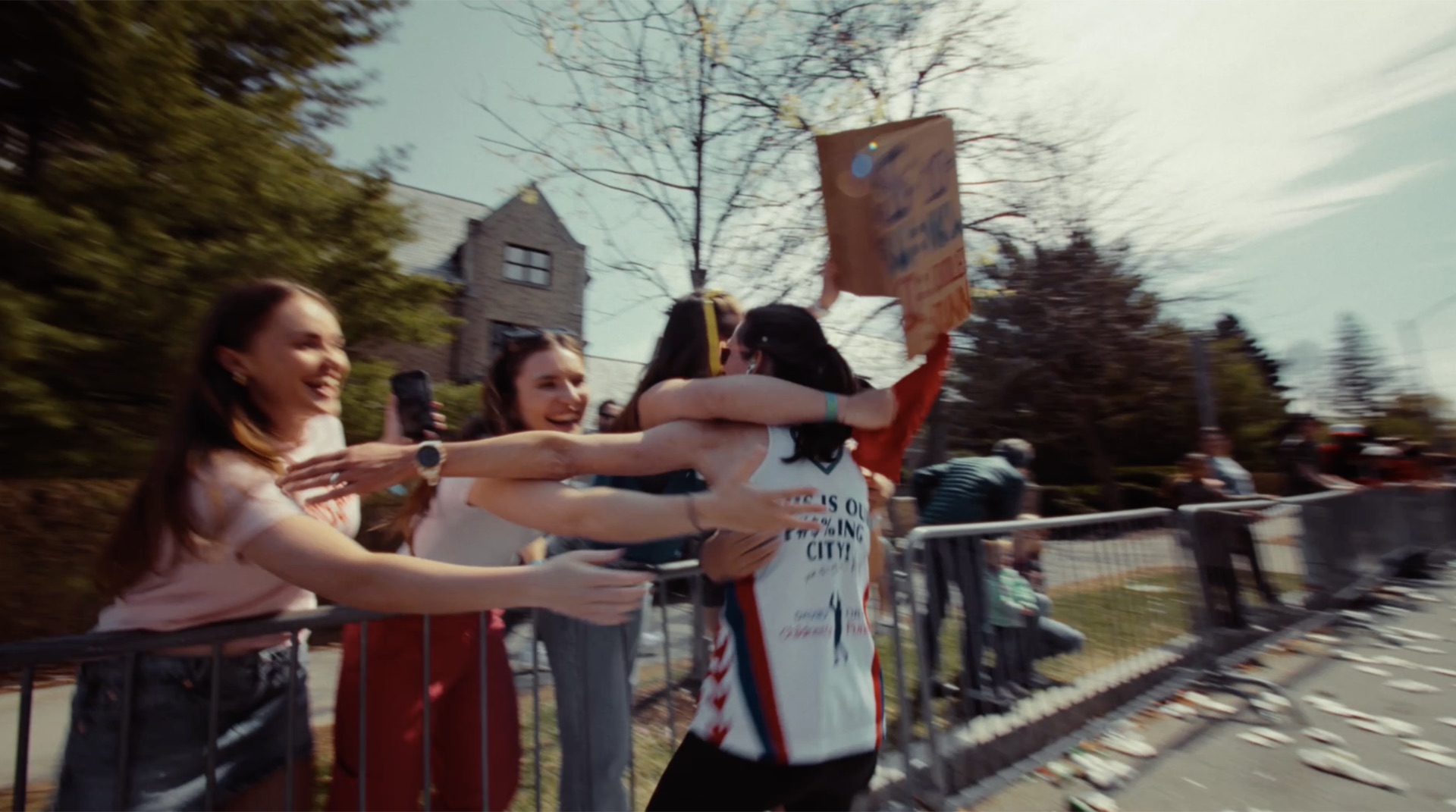 Runner embracing a friend at the barricades, spectators cheering with a handmade sign