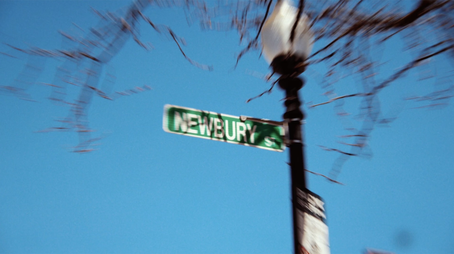 Motion-blurred shot of the Newbury St. street sign against a clear blue sky
